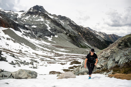 A women hikes up a snow field on a summer day in the mountains for British Columbia.