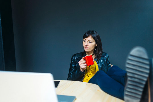 Young woman is drinking hot beverage at workplace.