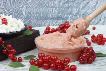 Cream honey on a spoon spindle with the taste of red currant, next to a bunch of berries and grain curd