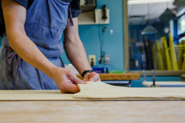 Close-up of baker folding pastry dough on floured surface in kitchen