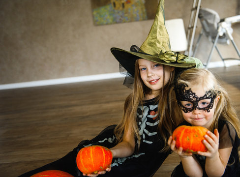 Two Sisters Dressed for Halloween in Skeleton Costumes with Pumpkins