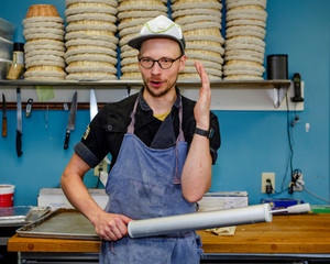 A professional baker talks with rolling pin in hand in kitchen