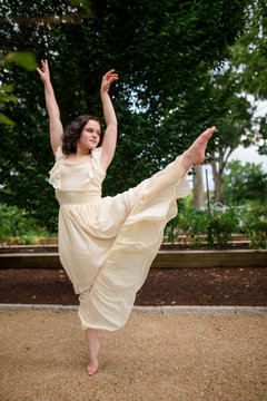 A dancer in a long white dress dances on a gravel path in a park