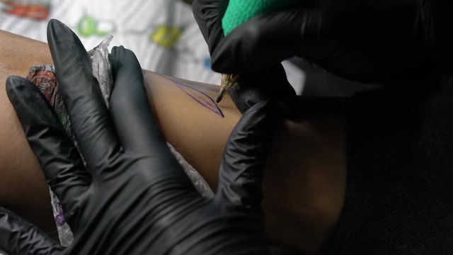 Tattoo female artist makes a tattoo on a female leg.