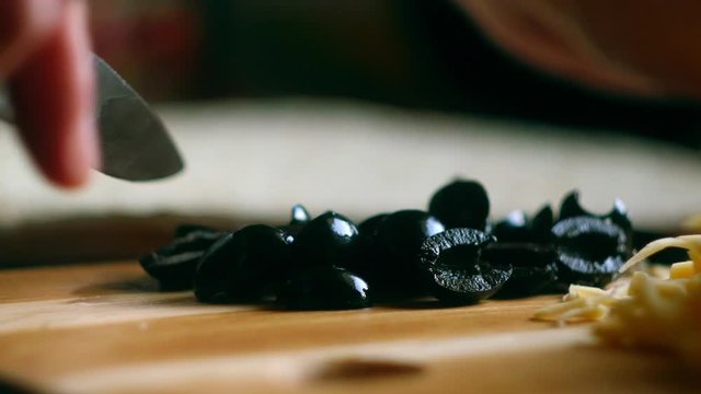 Close up cutting black olives on bamboo desk. Cooking process 