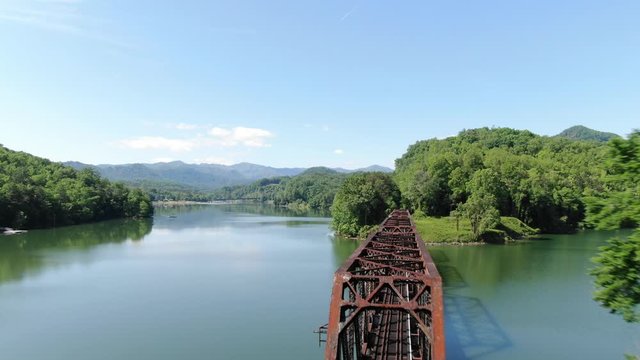 Low aerial above trestle traintrack bridge. Low flyby and reveal to green forested lake 4K Mavic 2 Zoom