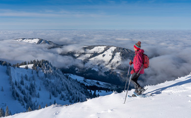 Fototapeta na wymiar nice senior woman snowshoeing on the Nagelfluh chain above a sea of fog over Bregenz Wald mountains, Hochgrat, Steibis,Bavarian alps, 