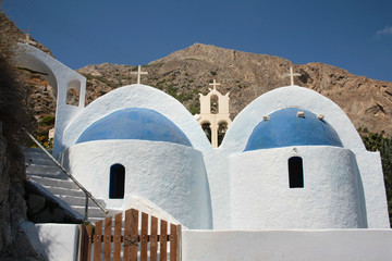 Charakterystyczy biało-niebieski kościół  na tle skalistych wzgórz wyspy Santorini - obrazy, fototapety, plakaty