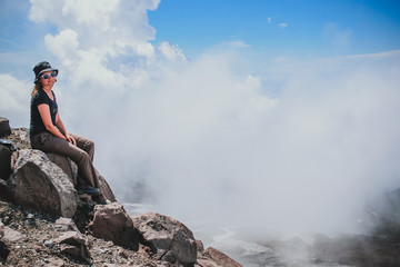 tourist girl sitting on a peak on stones among clouds high above sea level while climbing Avachinsky volcano in Kamchatka in the far east of Russia 