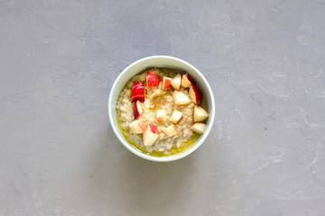 Breakfast of oatmeal porridge with butter and chopped red apples in a blue bowl on a concrete background, free space, top view