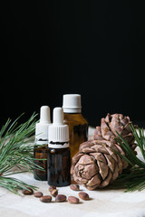 natural product, glass bottles with oil, pine cones with nuts on a tablecloth on a black background, close-up