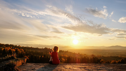 The boy enjoys the sunset in the mountains