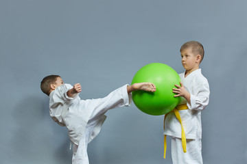 Little athlete performs a kick on a green ball on a gray background