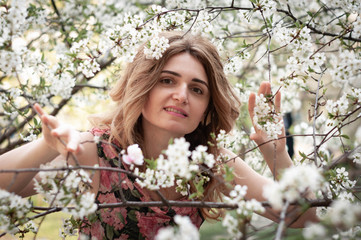 Fototapeta premium soft focus of attractive woman surrounded by blooming cherry flowers passing through tree branches and looking at camera in sunny garden