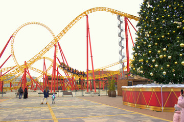 The roller coaster ride with thrill-seekers on the background of the New Year tree. Christmas...