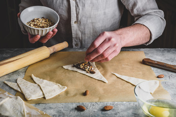 Croissant preparing. Baker sprinkles chopped almonds on top of hazelnut spread