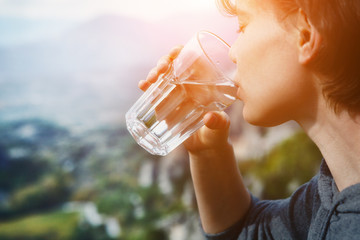 young woman holding glass of crystal clear natural water, drinking, nature mountain background