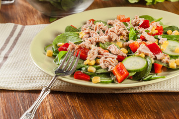 Fresh spinach salad with tuna, cucumber, corn, and red paprika on a plate