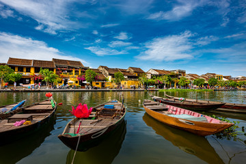 Fototapeta na wymiar Fishing boats on the Thu Bon River with old yellow buildings in Hoi An Vietnam