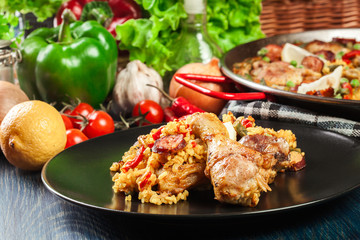 Traditional paella with chicken legs, sausage chorizo and vegetables served on black plate