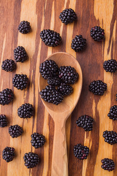 Wooden rustic tablespoon with blackberries. Scattered blackberries on wooden table, top view.