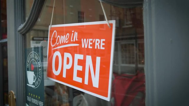 Woman Entering British Cafe With Signage Come In We're Open Large Sign Hanged At The Door
