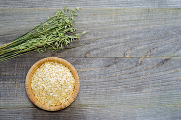 Oatmeal flakes in a bamboo bowl with green oats on an old faded gray wooden table background.
