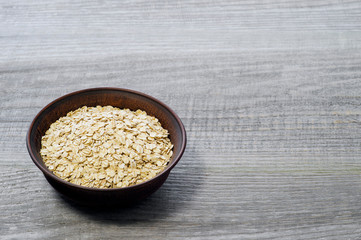 Oatmeal flakes in a deep ceramic brown dark bowl on an old faded gray wooden table background.