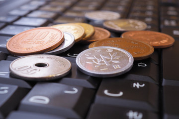 A pile of different Japanese coins lies on a black keyboard of a computer or laptop. Denomination is 1, 10, 50 yen. Online trading, payments and remote work. Macro