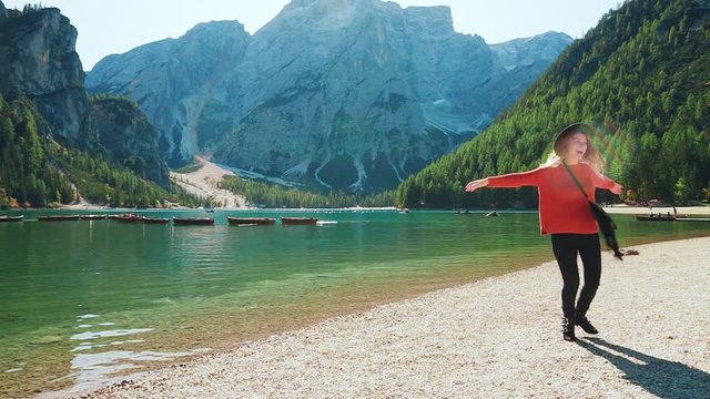 happy young woman tourist whirls dancing with open hands enjoying wild nature. Backdrop white mountains Dolomites Alps, turquoise Lake Braies, green forests. Positive emotions amazing view landscape