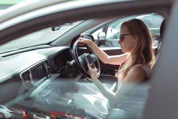 woman in car, sitting behind wheel of a car, reads and writes message in mobile phone, parking mall, traffic jam, in summer in car. Girl in pink dress, automatic transmission.