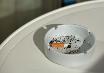 Niedopałek papieros / pet, popiół, w białej popielniczce na stole, z bliska