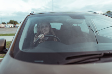 woman in car, sitting behind the wheel of a car, happy smile, right wheel of car, left-hand traffic. Windshield, fall day outside. Free space for copy text.