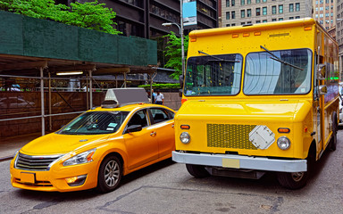 Yellow taxi and school bus on road. Street view in Financial District of Lower Manhattan, New York of USA. Cityscape with skyscrapers at United States of America, NYC, US. American architecture.