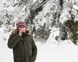 Fototapeta na wymiar Handsome young man looking at camera and drinking coffee with thermos mug and enjoying snow in winter season. Winter in Eskisehir.