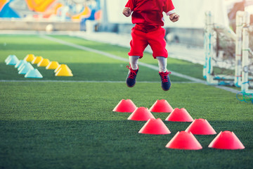 Obraz premium Kid soccer player Jogging and jump between red cone markers on green artificial turf for soccer training. Football or soccer academy.