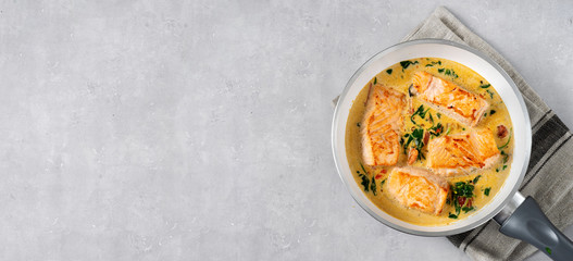 Salmon steaks in a frying pan with cream on light background