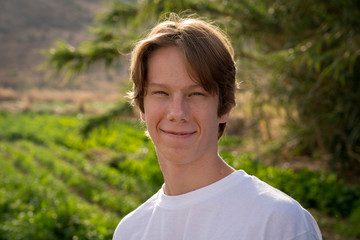A teenage boy smirks at the camera while backlight in the afternoon sun.
