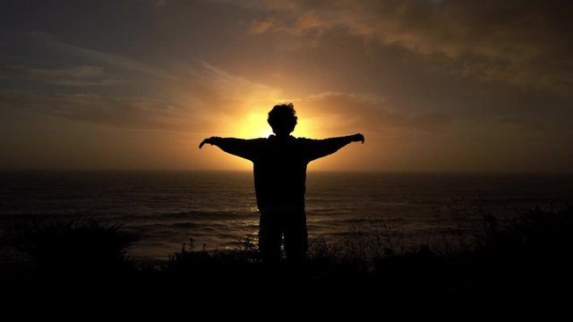 This stock video shows the silhouette of a man raising his arms against the sunset.