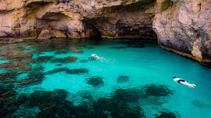 Swimmers snorkel in the warm clear mediterranean waters of the blue lagoon near Comino in Malta.