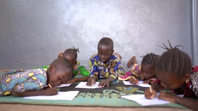 Four Smart Little African Children Lying on The Floor Writing On A Sheet of Paper