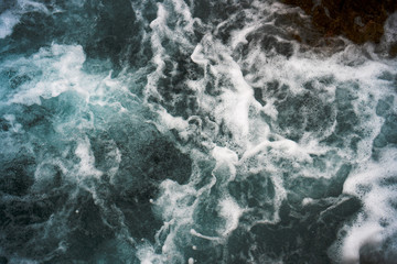 Fototapeta na wymiar Raging blue water in a backwater with stones and white foam.