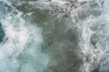 Fototapeta na wymiar Raging blue water in a backwater with stones and white foam.