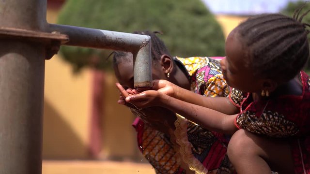 Two beautifully Dressed Little African Girls Sipping Water From a Tap