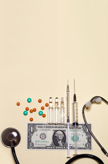 vertical of medical supplies, stethoscope, syringe, ampoule, tablet on one american dollar banknote...