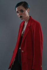 Studio photoshoot of a beautiful girl with blue hair and fashion makeup in a red jacket on a grey background. Fashion style