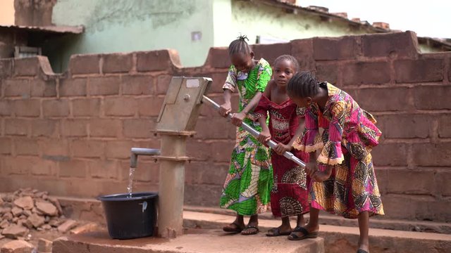 Three Little African Girls Pumping Water At The Community Well
