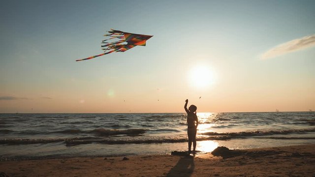 Happy little girl playing with the kite on a sunny day. Young cute child playing with a colorful kite on the tropical beach. Concept of sea vacation.