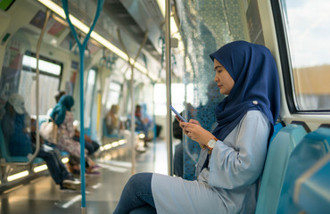 Young Muslim woman traveling inside subway train sitting while using phone. Transportation and...