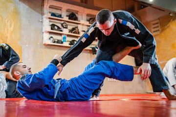 Two brazilian jiu jitsu BJJ athletes training practicing position drilling the technique from the guard sparring wearing blue and black kimono gi de la riva sleeve - obrazy, fototapety, plakaty